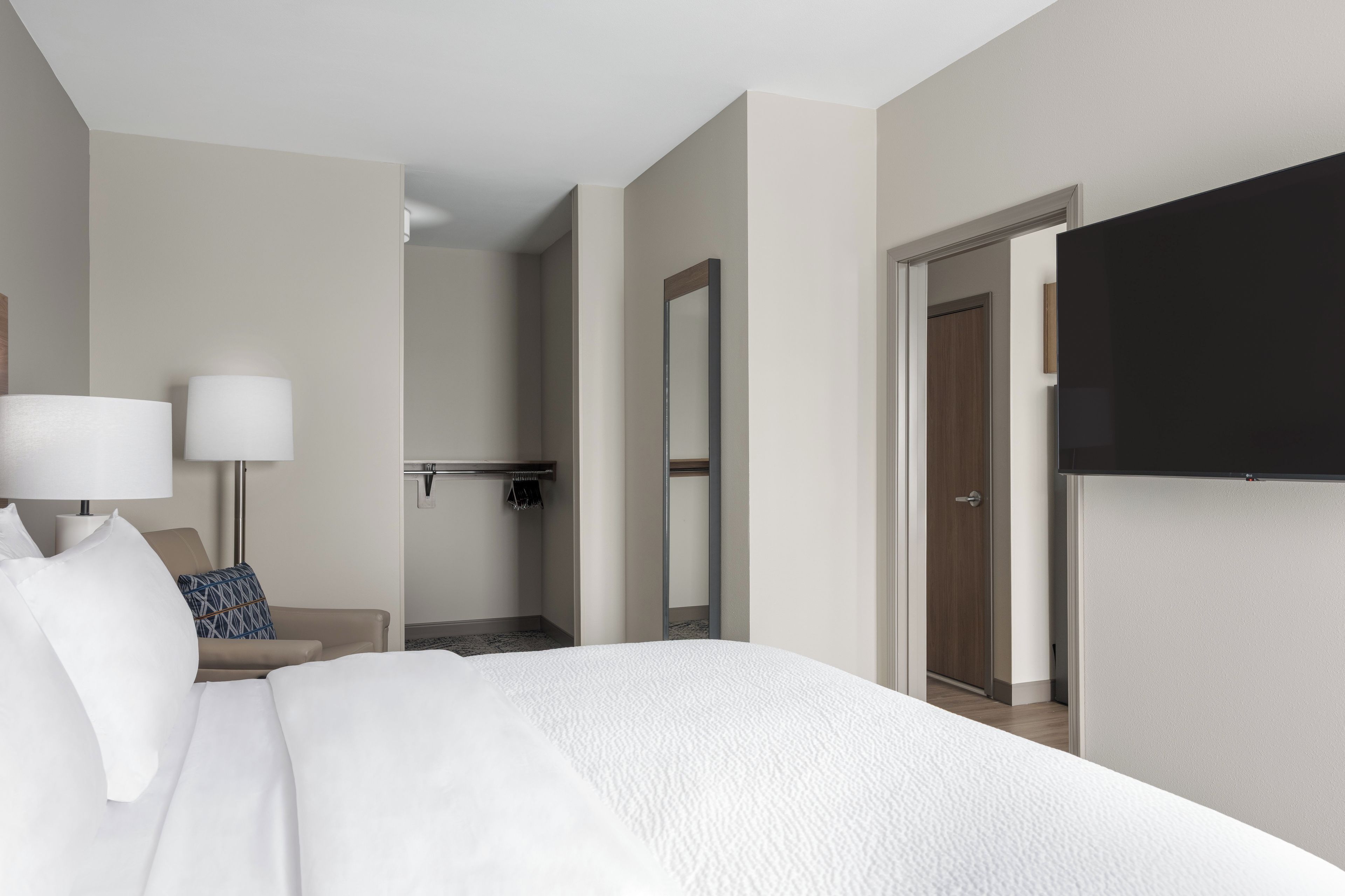 A hotel room with a bed, a desk, a chair, a TV, and a bathroom visible through an open door.