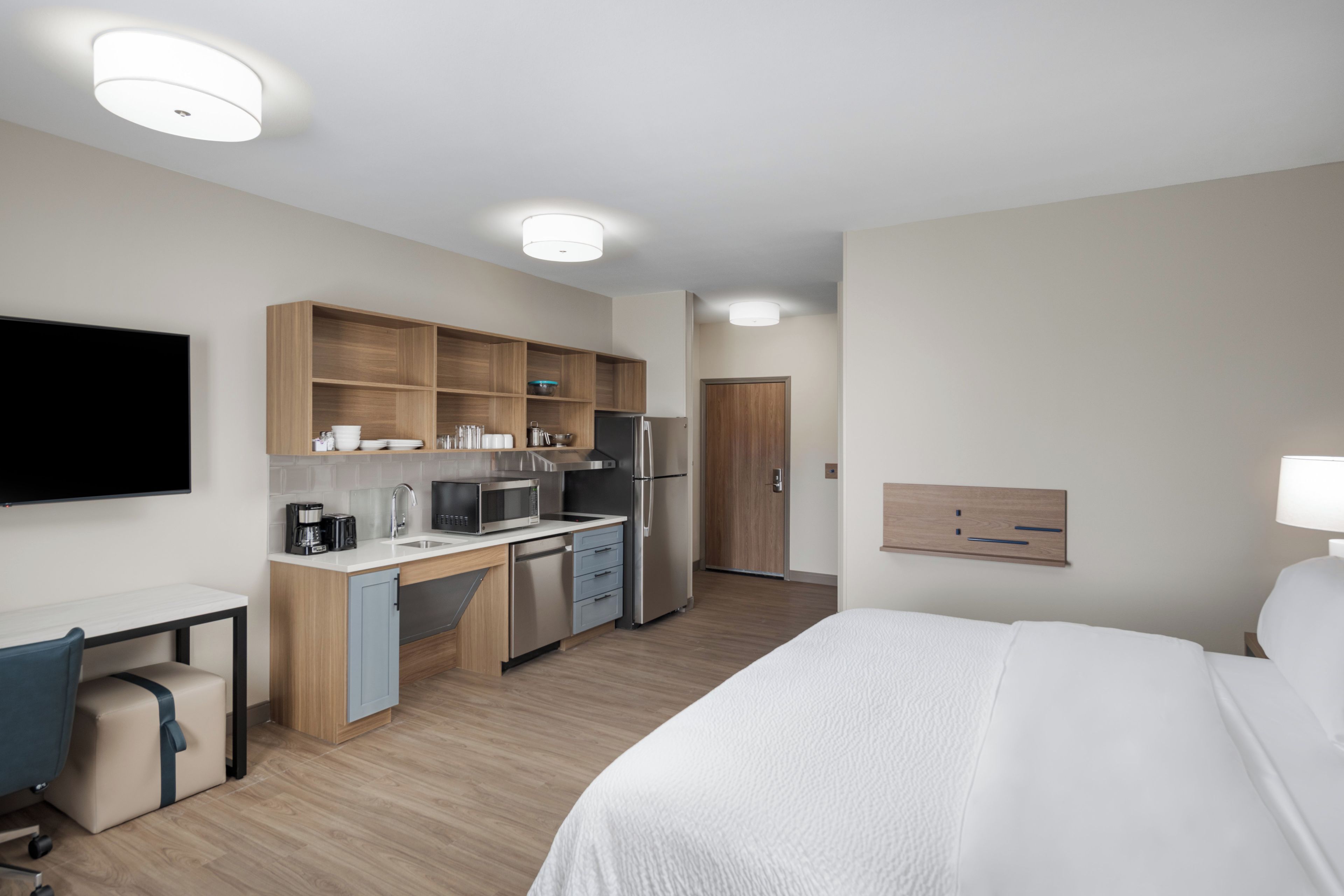 A hotel room with a bed, a desk, a kitchenette, and a TV.