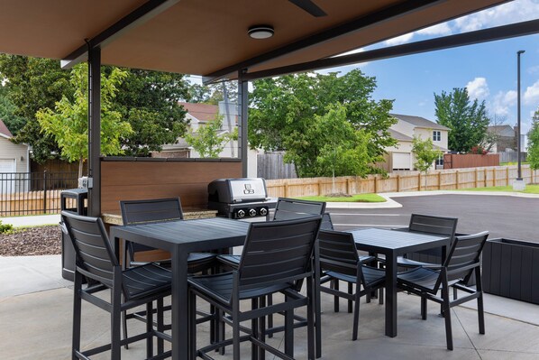 Un patio al aire libre con una parrilla, mesas y sillas.