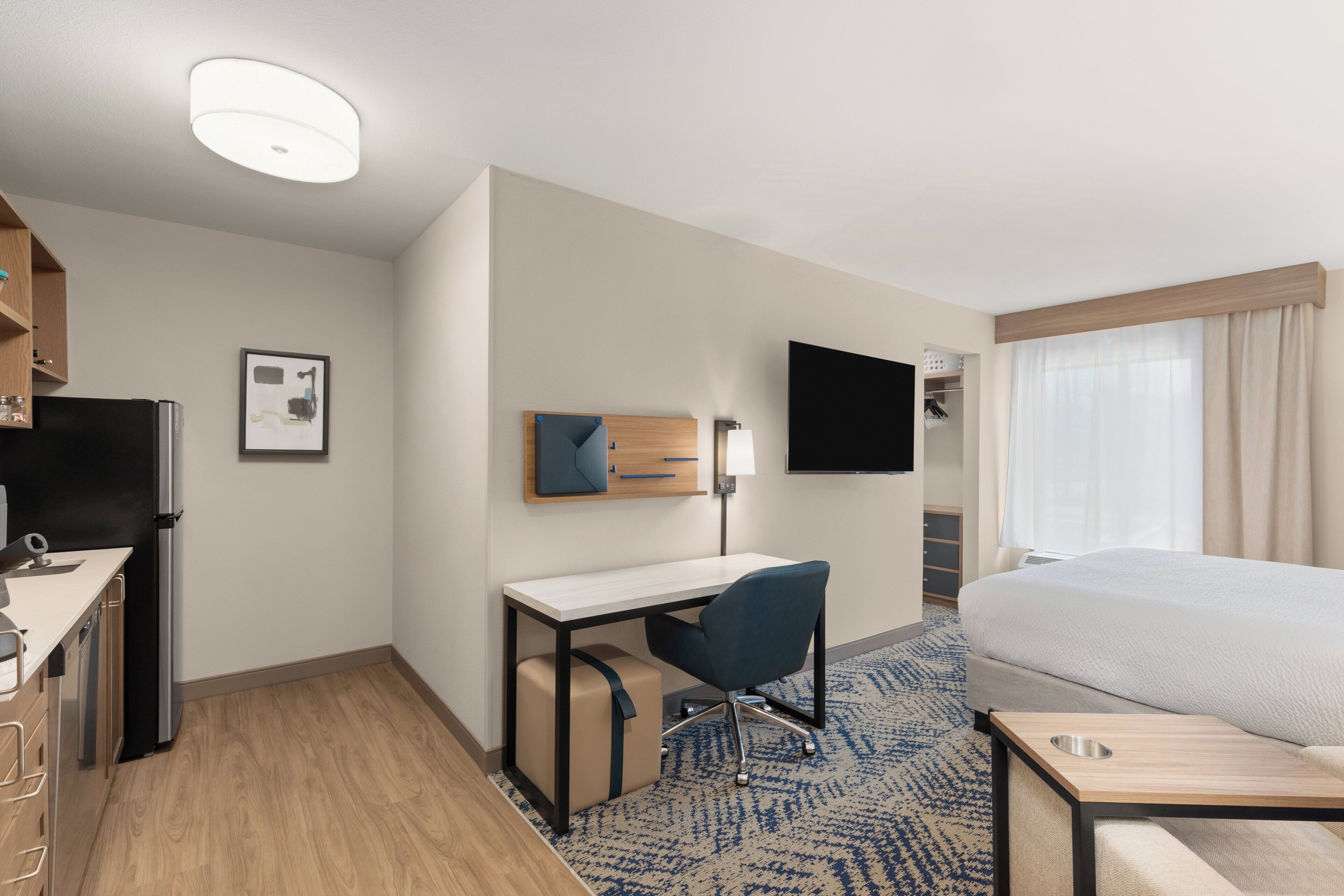 A hotel room with a bed, desk, chair, TV, and a refrigerator.