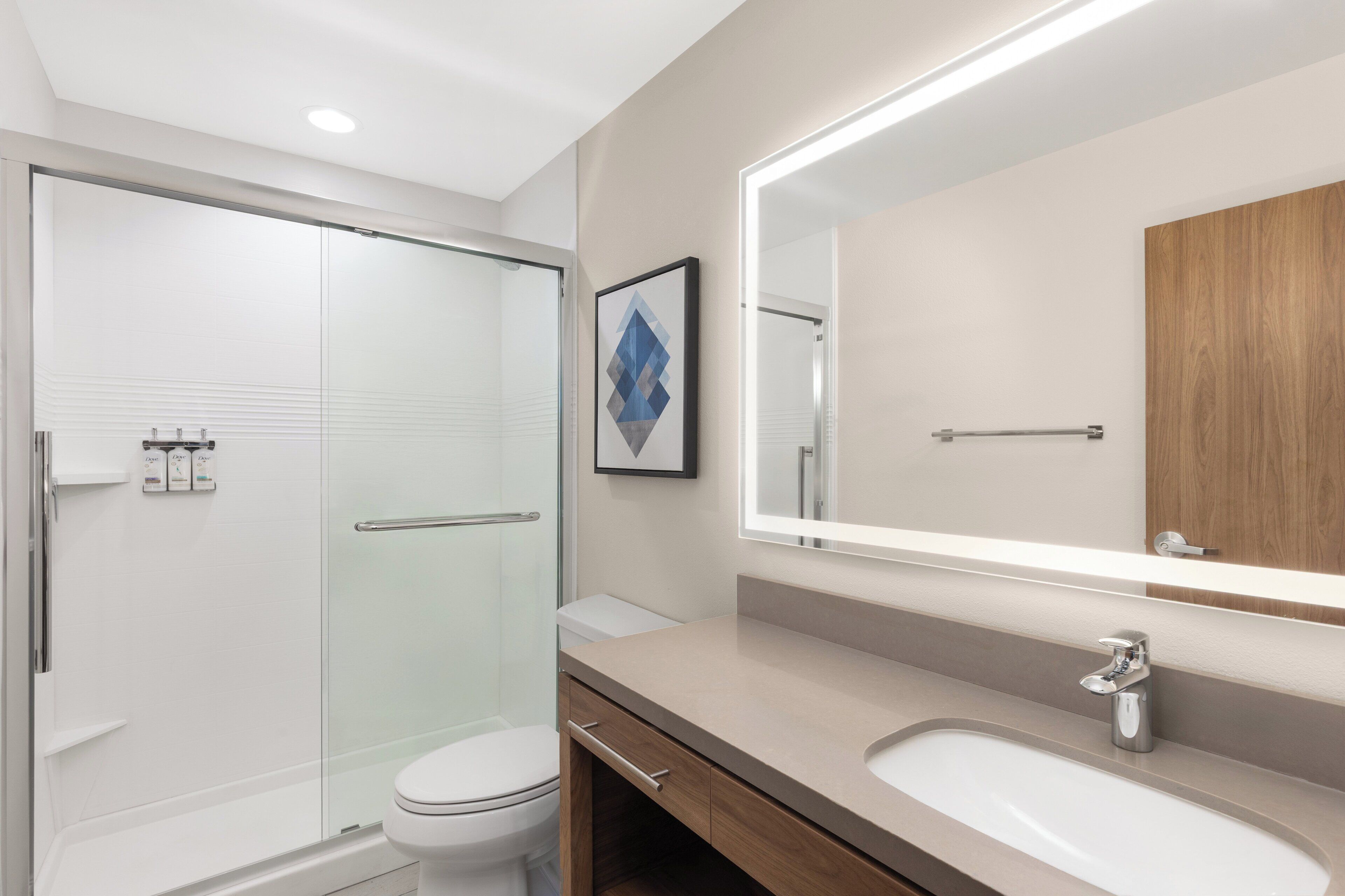 Un baño moderno con cabina de ducha de vidrio, inodoro, tocador con espejo y lavabo.