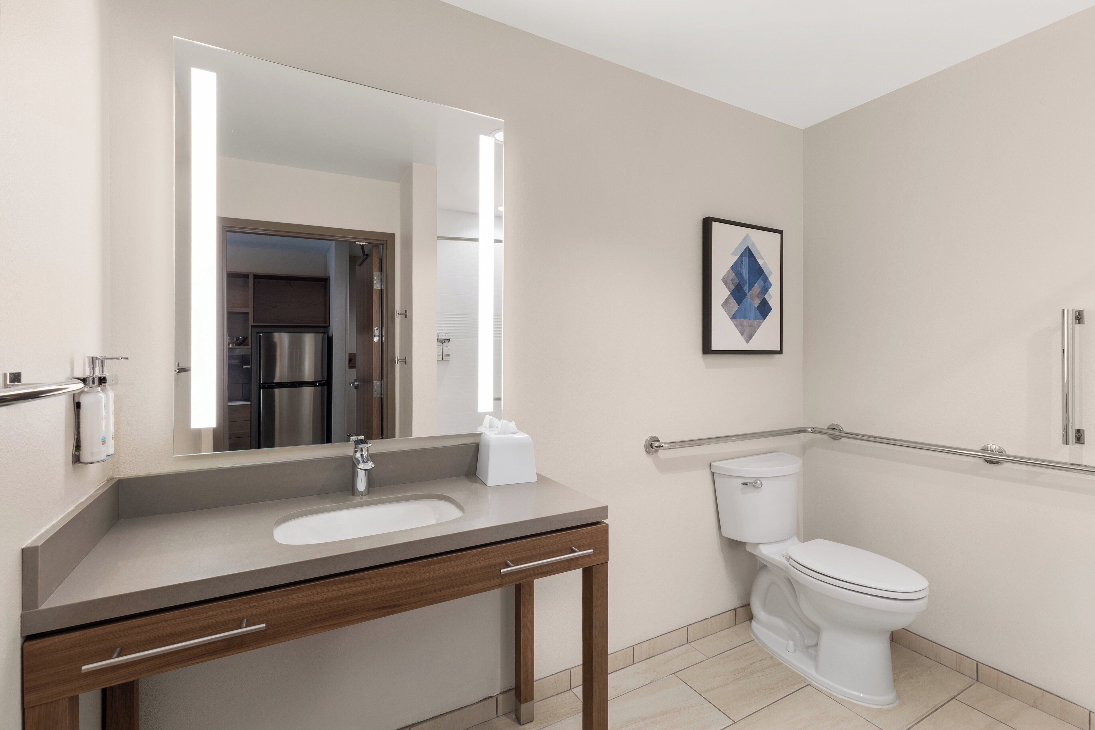Un baño moderno con lavamanos, espejo, inodoro y barras de apoyo.