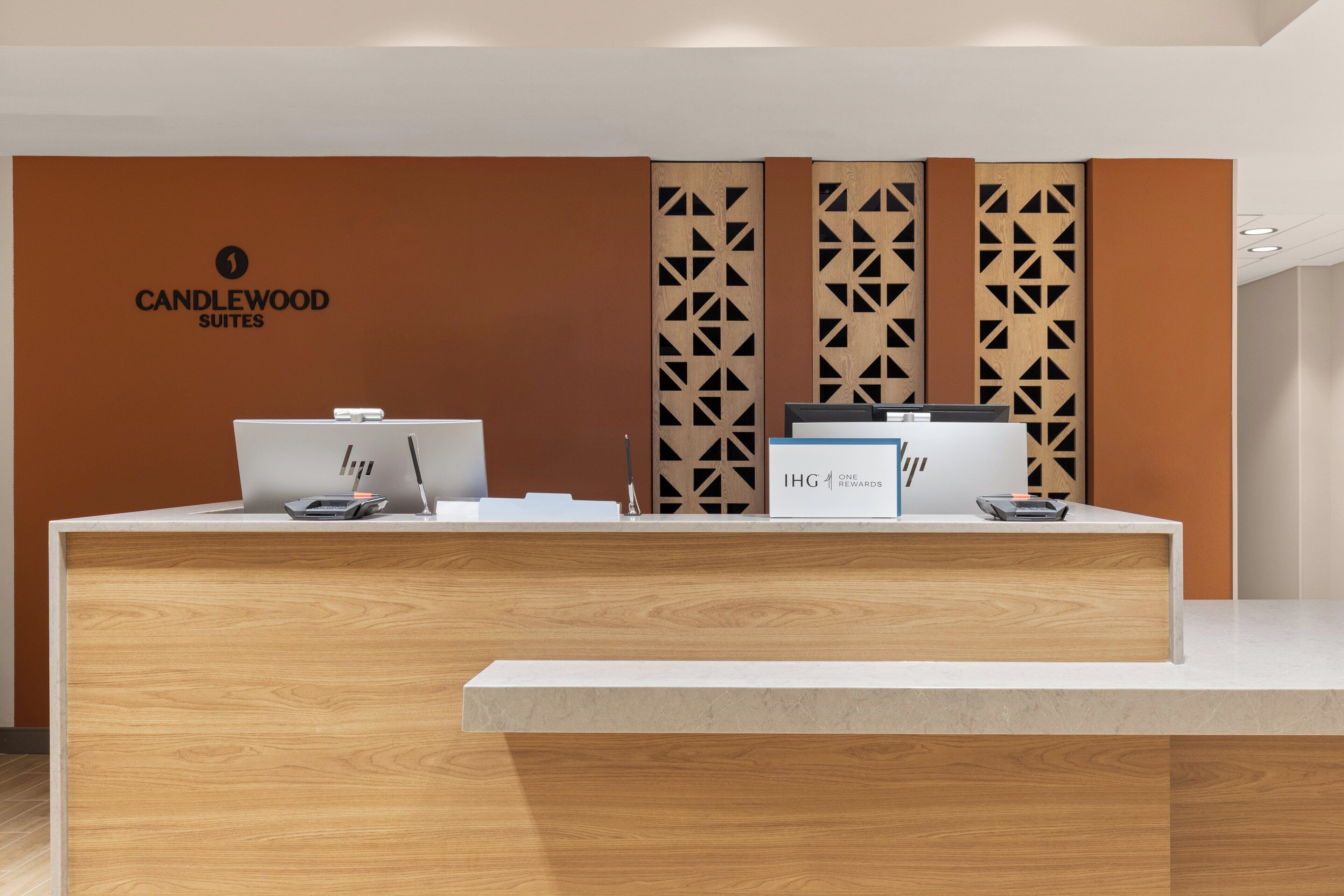 A reception desk with a logo for Candlewood Suites, a computer, a printer, and a sign for IHG Rewards.