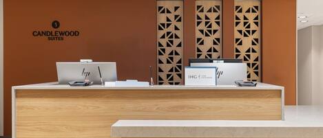 A reception desk with a logo for Candlewood Suites, a computer, a printer, and a sign for IHG Rewards.
