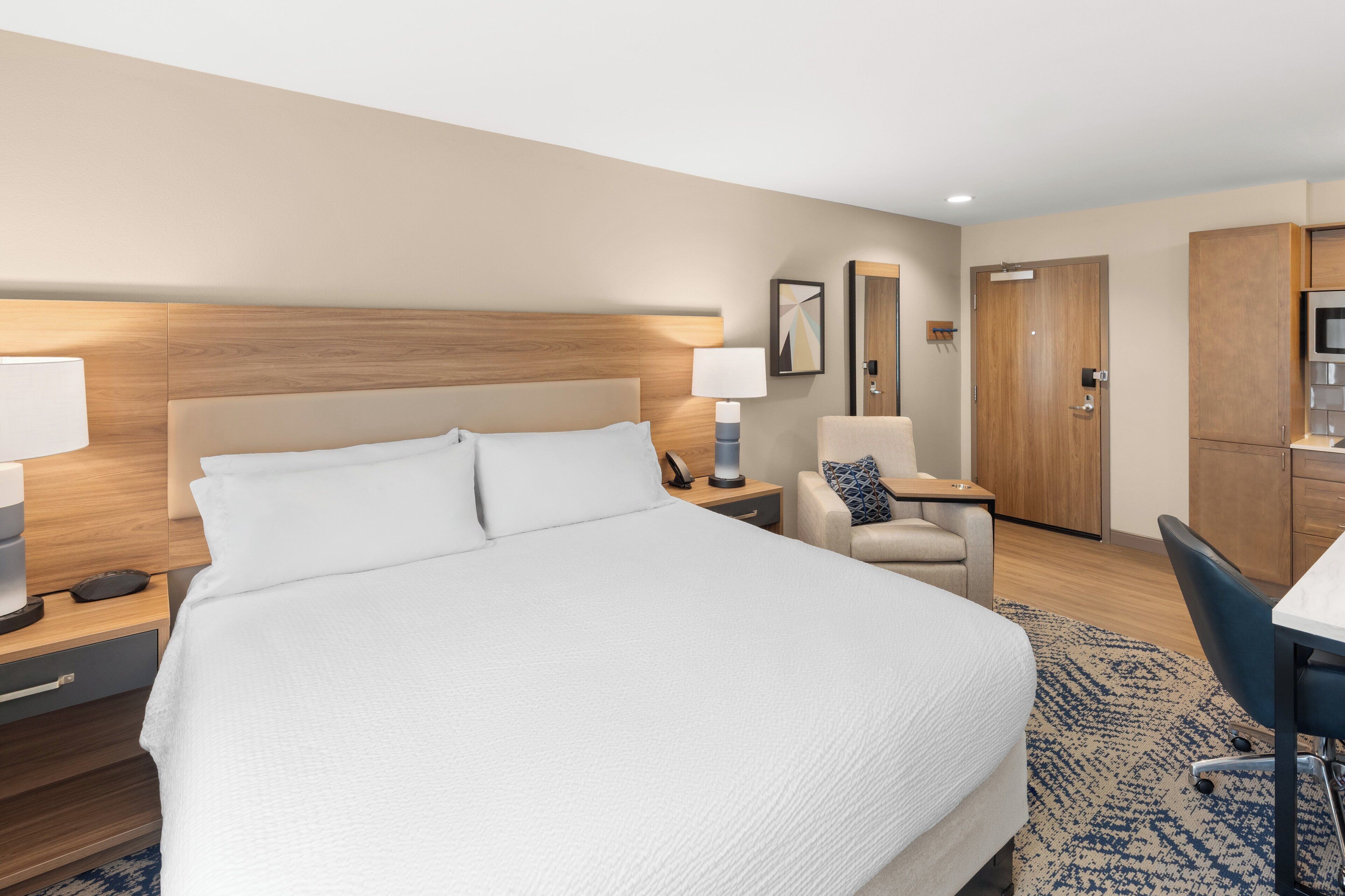 A hotel room with a large bed, bedside tables, a desk, a chair, and a wardrobe.