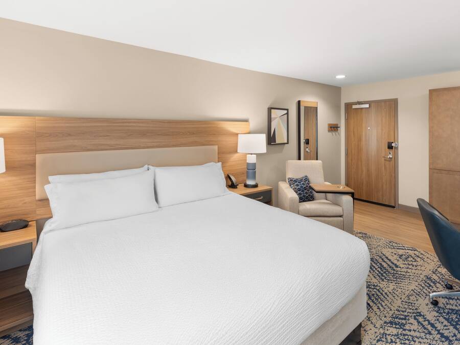 A hotel room with a large bed, bedside tables, a desk, a chair, and a wardrobe.