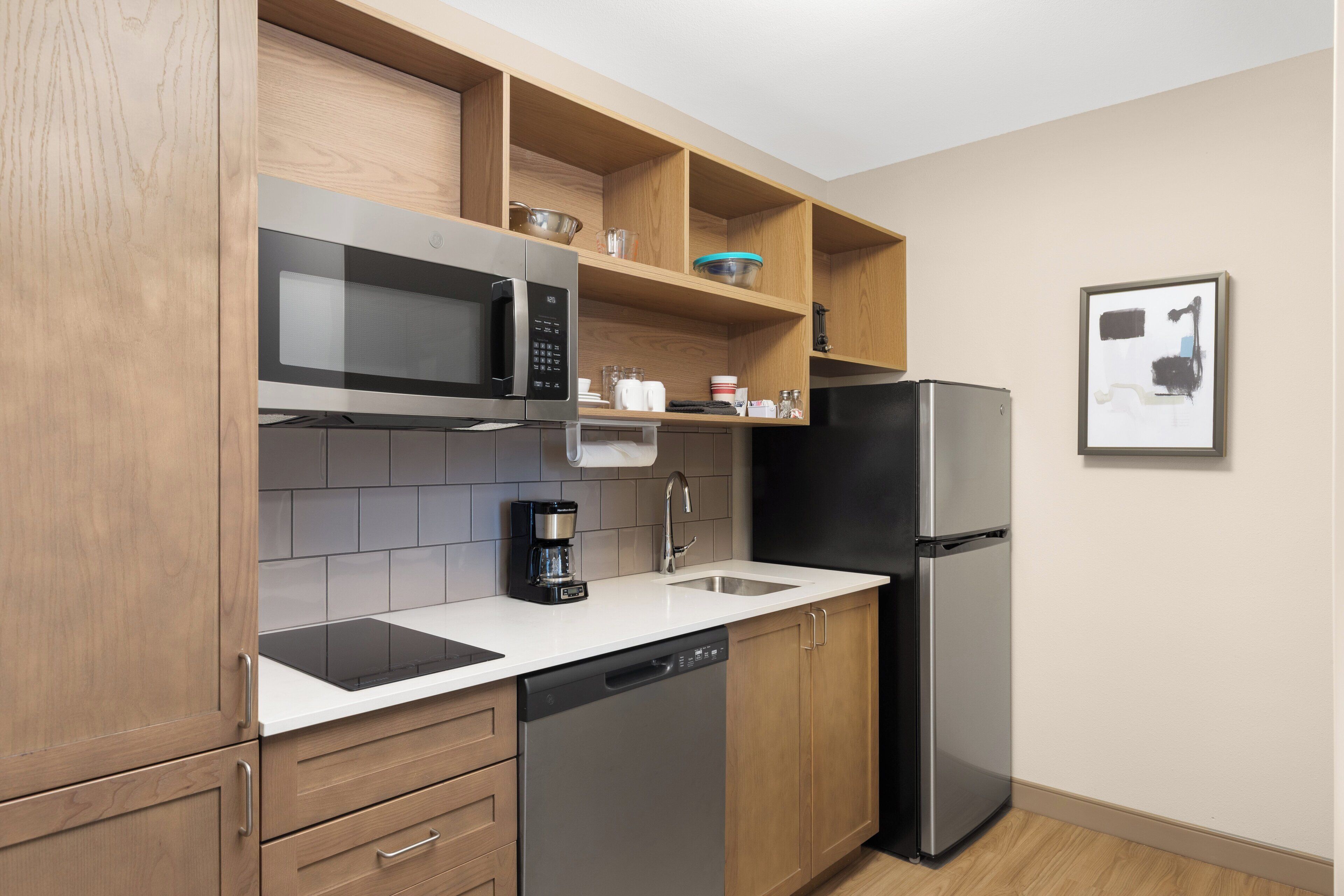 A modern kitchen with wooden cabinets, a stainless steel refrigerator, a microwave, and a dishwasher.