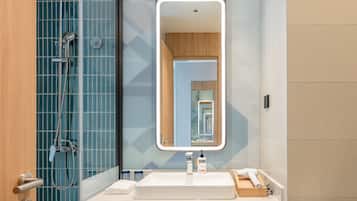 Une salle de bain moderne avec un grand miroir, une douche et un lavabo équipé de produits de toilette.