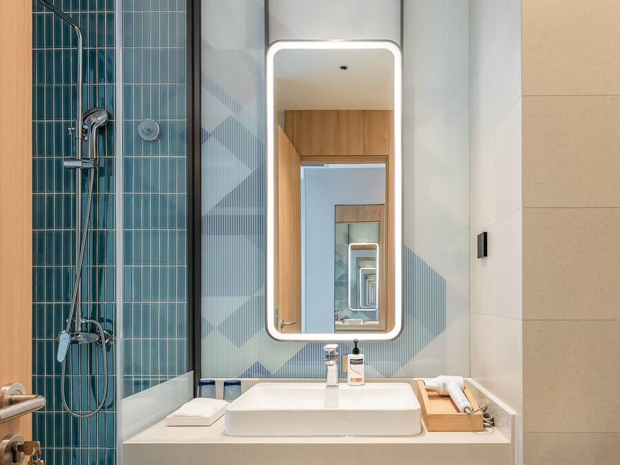 Une salle de bain moderne avec un grand miroir, une douche et un lavabo équipé de produits de toilette.