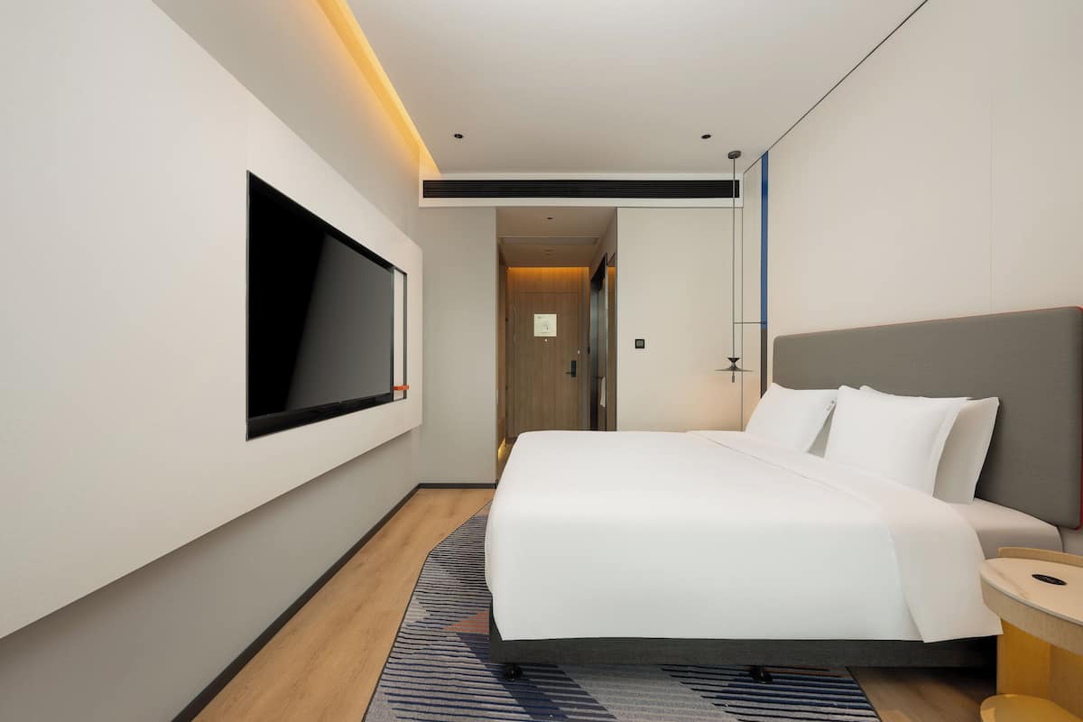 Ein modernes Hotelzimmer mit einem großen Bett, einem flachbildfernseher an der Wand und Holzboden.