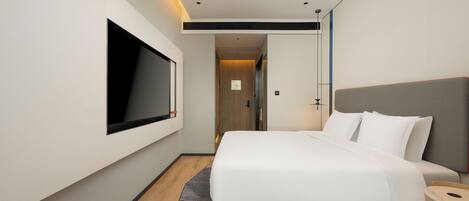 A modern hotel room with a large bed, a flat-screen TV mounted on the wall, and a wooden floor.