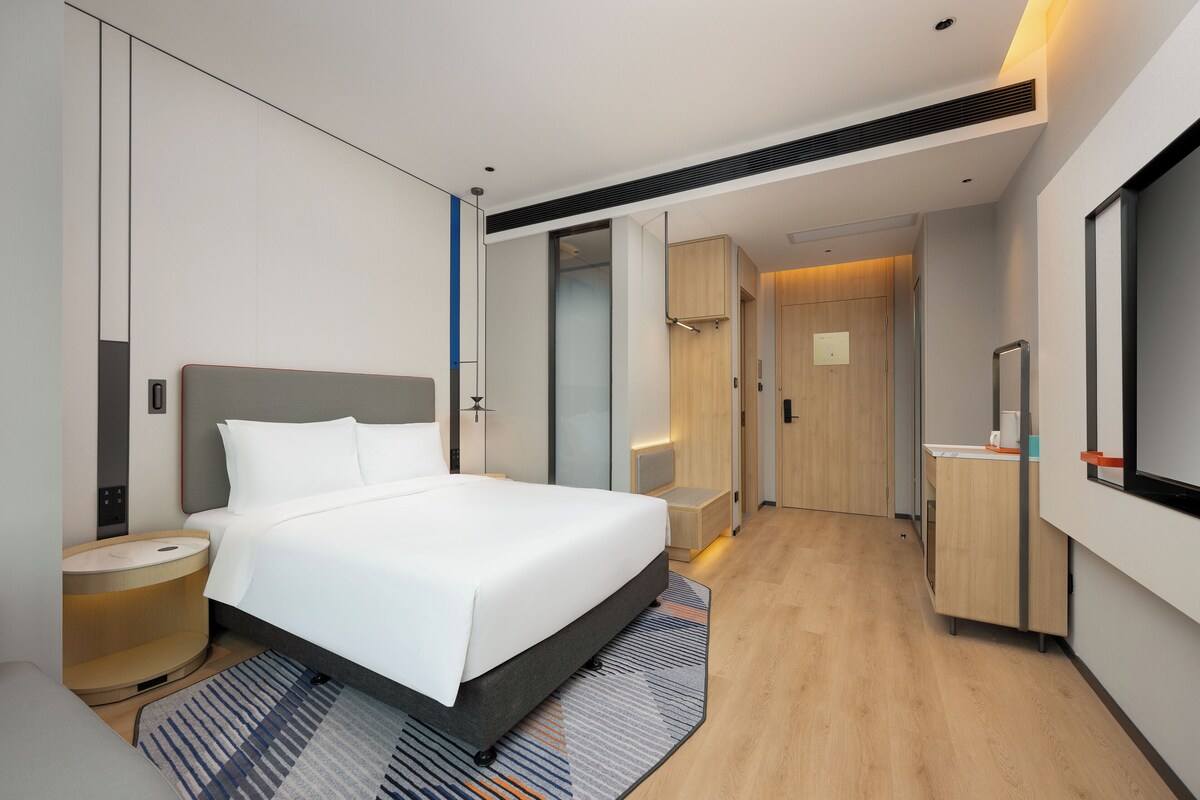 Ein modernes Hotelzimmer mit einem großen Bett, Nachttischen, einem Spiegel und einem begehbaren Kleiderschrank.