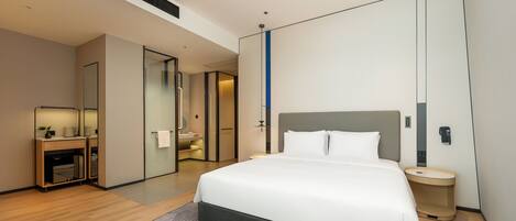 Ein modernes Hotelzimmer mit einem großen Bett, einem Nachttisch, einem Spiegel und einer kleinen Sitzecke mit einer Pflanze.