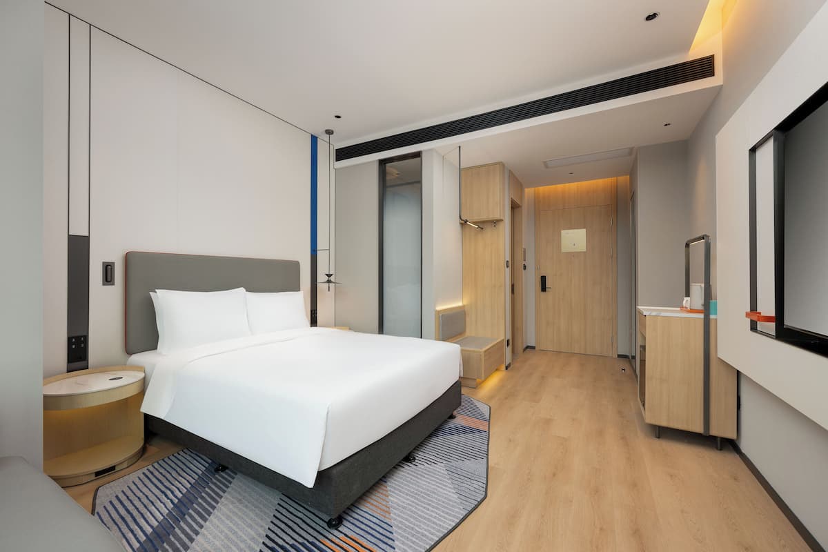 Ein modernes Hotelzimmer mit einem großen Bett, Nachttischen, einem Spiegel und einem begehbaren Kleiderschrank.