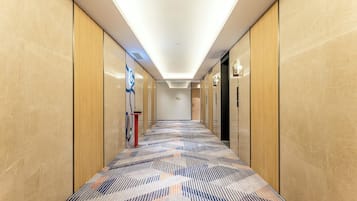 A hotel hallway with a patterned carpet, wooden panel walls, and a ceiling light fixture.