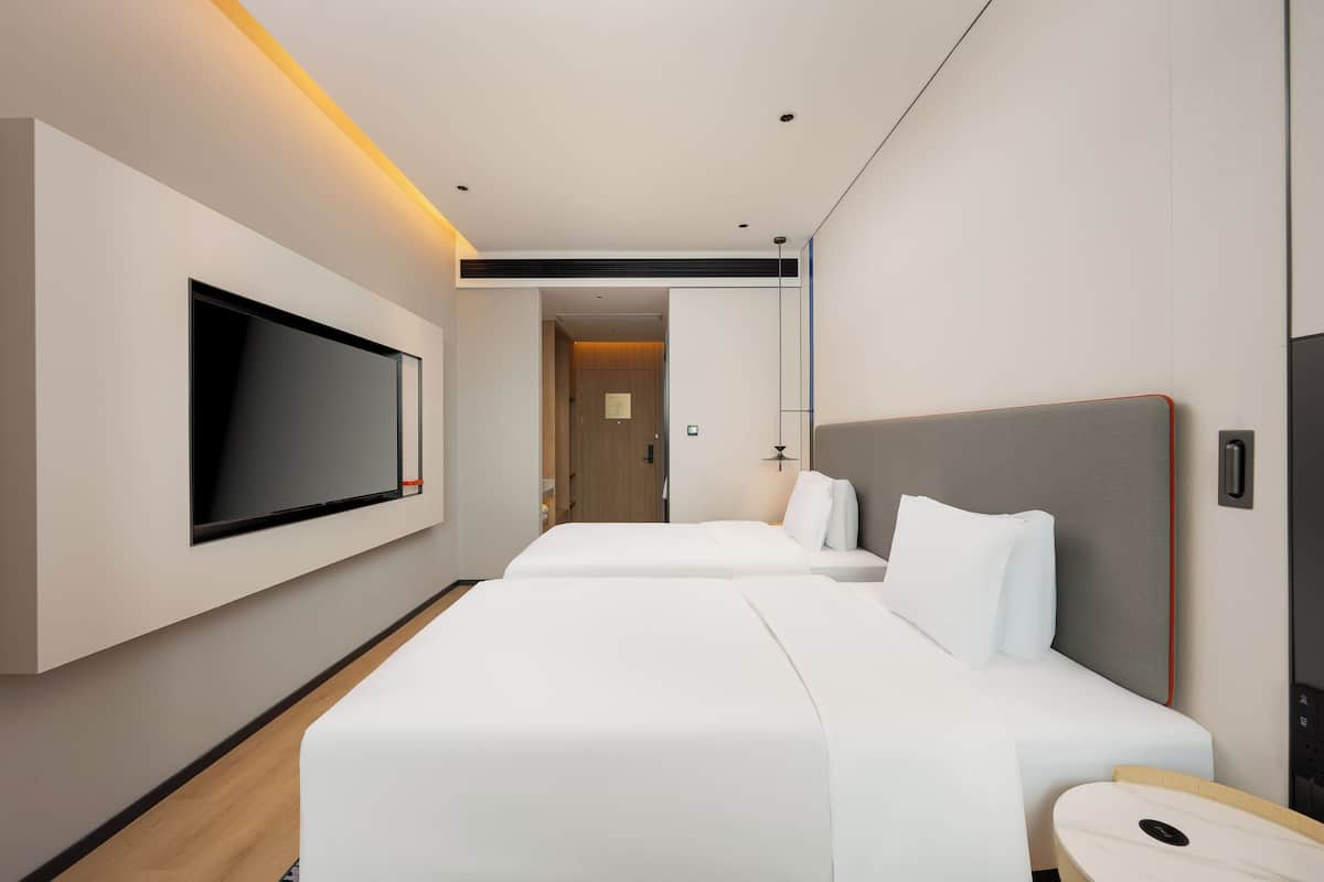 Ein modernes Hotelzimmer mit zwei Betten, einem flachbildfernseher an der Wand und Holzboden.