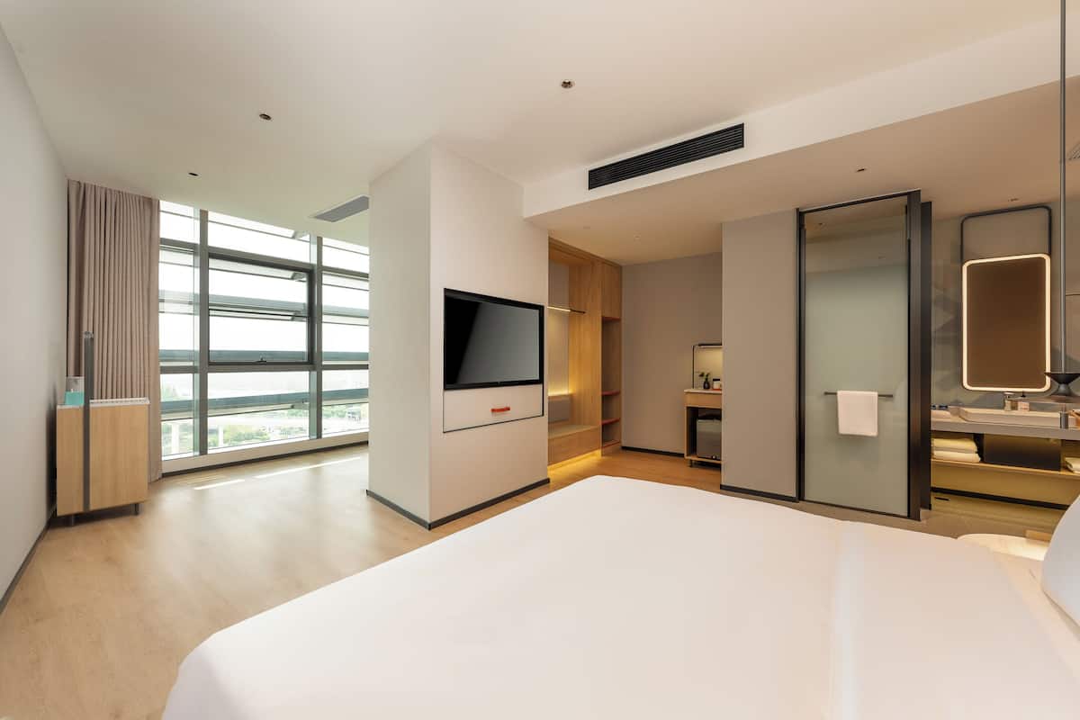 Ein modernes Hotelzimmer mit einem großen Bett, einem Flachbildfernseher, einem Schreibtisch und einem Badezimmer mit Spiegel und Waschbecken.