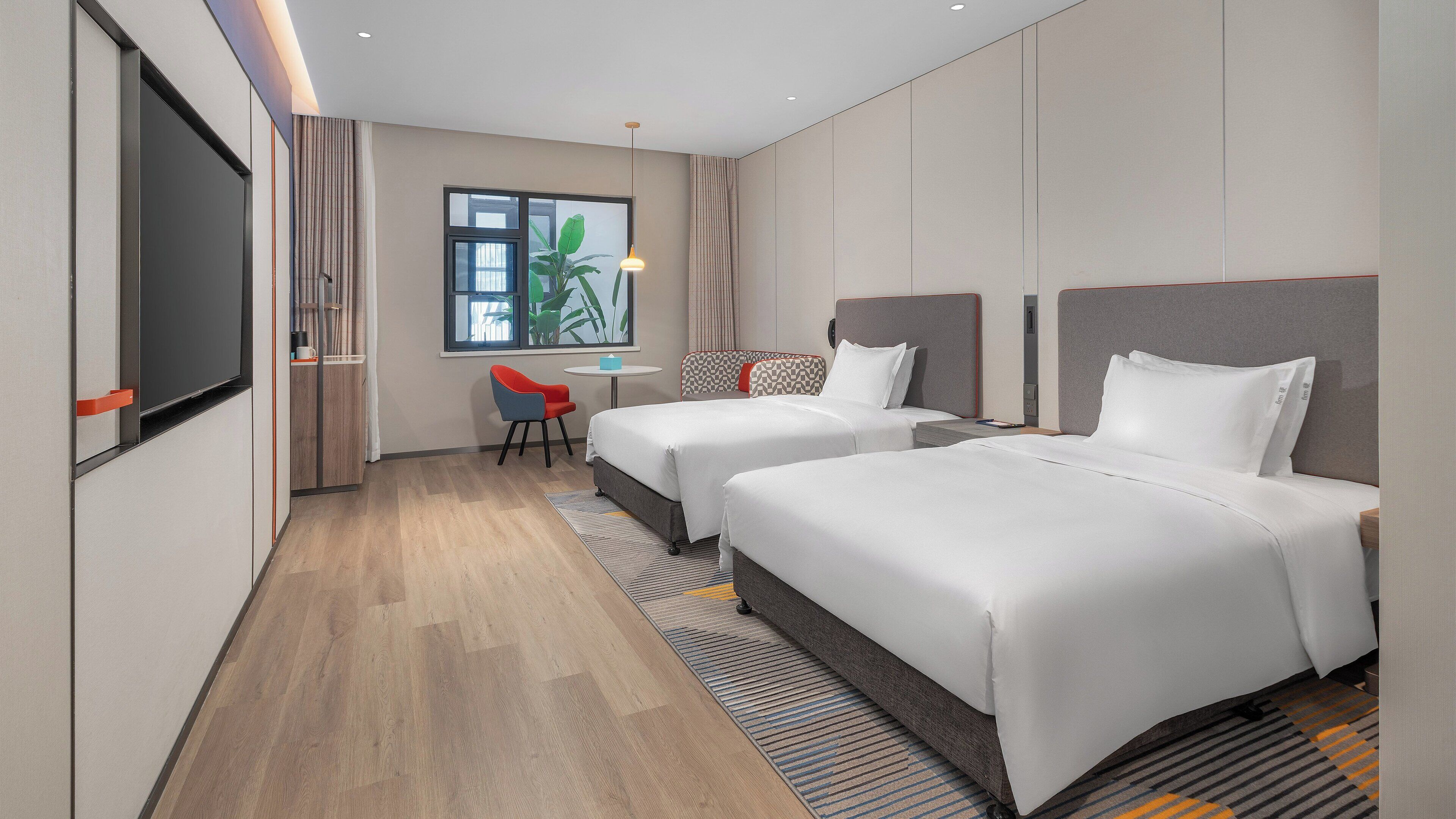 A hotel room with two beds, a small table, a chair, and a TV.