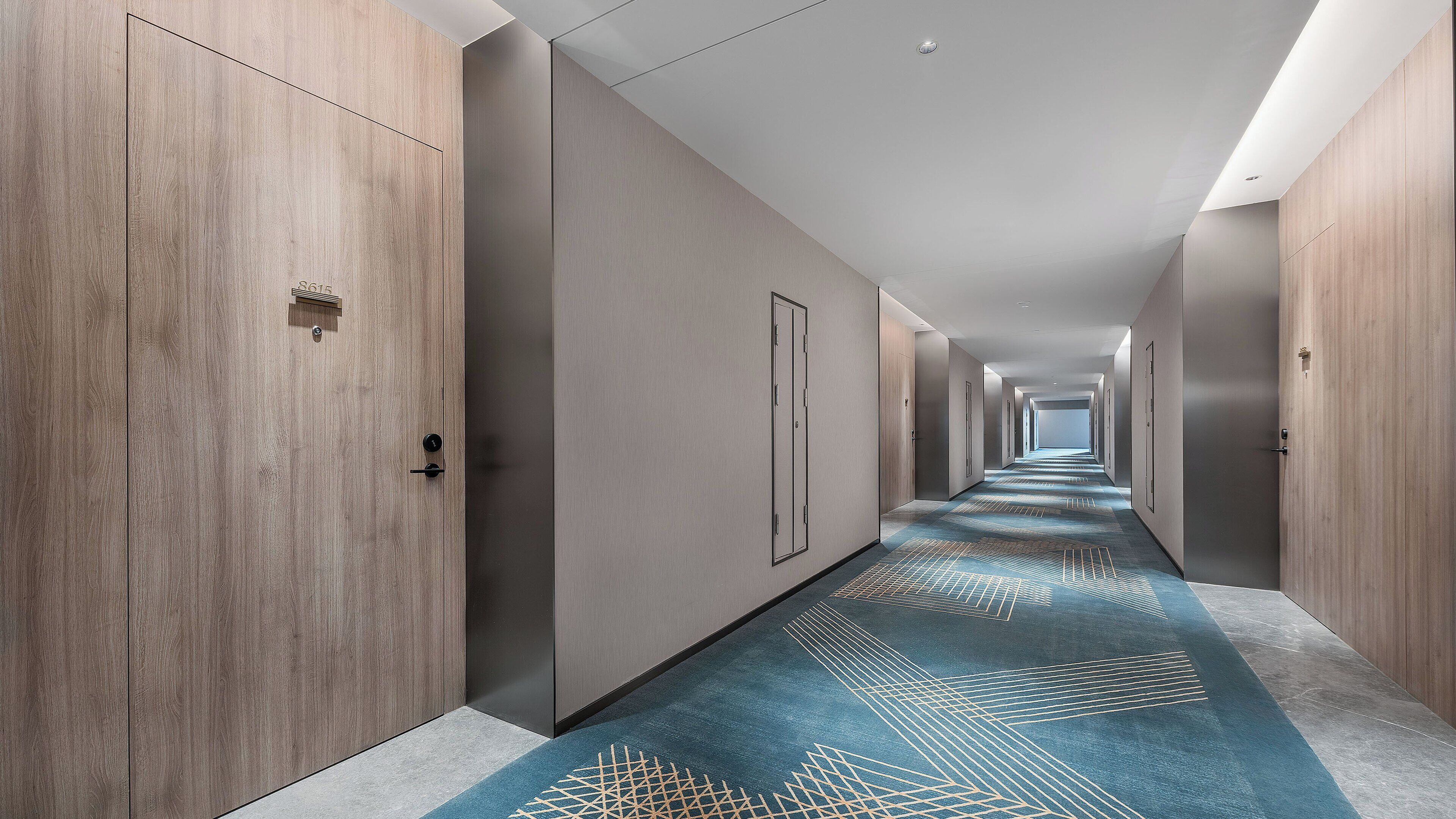 Un couloir d’hôtel avec des portes en bois, une moquette à motifs et un long couloir.
