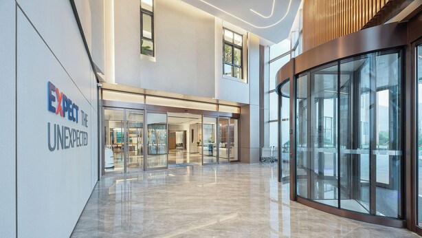 Un hall d’entrée moderne avec des portes en verre, un comptoir d’accueil et une enseigne sur laquelle on peut lire : « PRÉPAREZ-VOUS À L’INATTENDU ».