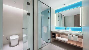 Um banheiro moderno com box de vidro, vaso sanitário branco, pia com bancada iluminada em azul e um espelho grande.