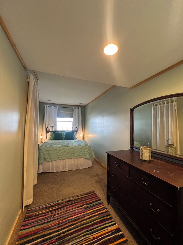 Une chambre à coucher avec un lit, une commode, un miroir et une fenêtre avec des rideaux.