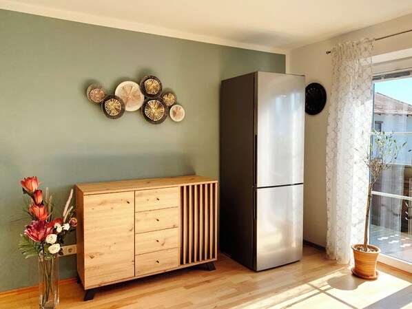 Una cocina moderna con un armario de madera, un refrigerador de acero inoxidable, placas decorativas en la pared y una ventana con cortinas.