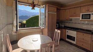 A kitchen with a view of mountains, a dining table, chairs, and basic appliances.