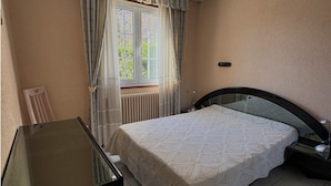 A bedroom with a bed, a desk, and a window with curtains.