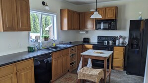 A kitchen with wooden cabinets, a black microwave, a refrigerator, and a window with a view of greenery outside.