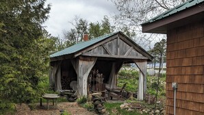 A rustic wooden structure with a sloped roof, surrounded by a gravel path and greenery.