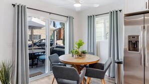 A modern kitchen with a built-in water dispenser, a round wooden table with chairs, and a sliding glass door leading to an outdoor area with a table and chairs. - Steps to Sand! 2 Homes in 1 Sleeps 17, Outdoor Space, Walk to Shops & Dining (Newport Beach)