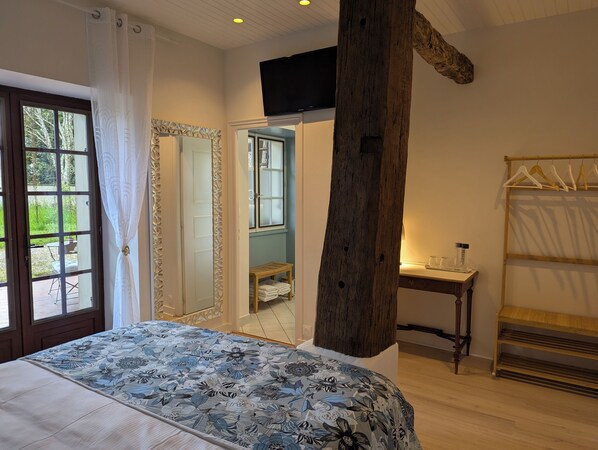 A bedroom with a large bed, a wooden beam, a TV, and a window with a view of greenery.