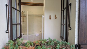 Une salle de bain avec une baignoire et une douche, une poutre en bois au plafond et un espace dédié aux plantes en pot.