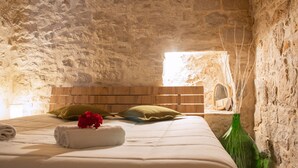 A stone-walled bedroom with a wooden headboard, a bed with white bedding, a green pillow, a rolled white towel, and a vase with branches. - The Aura Stone Room: an oasis of charm, nestled in the heart of Corato in Puglia. (Corato)