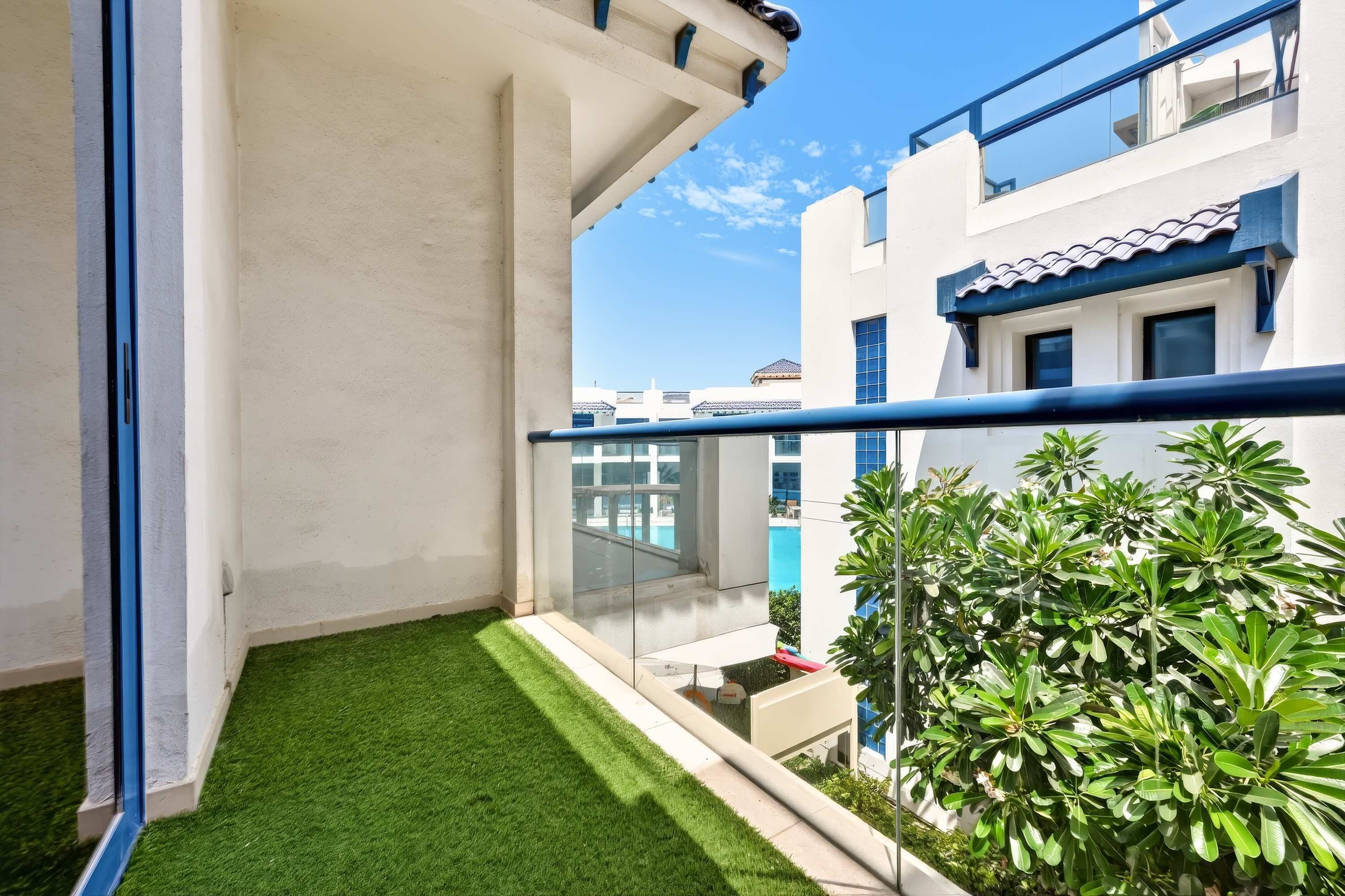 A balcony with artificial grass, a glass railing, and a view of neighboring buildings.