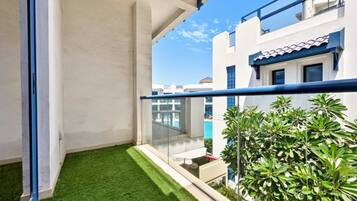 A balcony with artificial grass, a glass railing, and a view of neighboring buildings.
