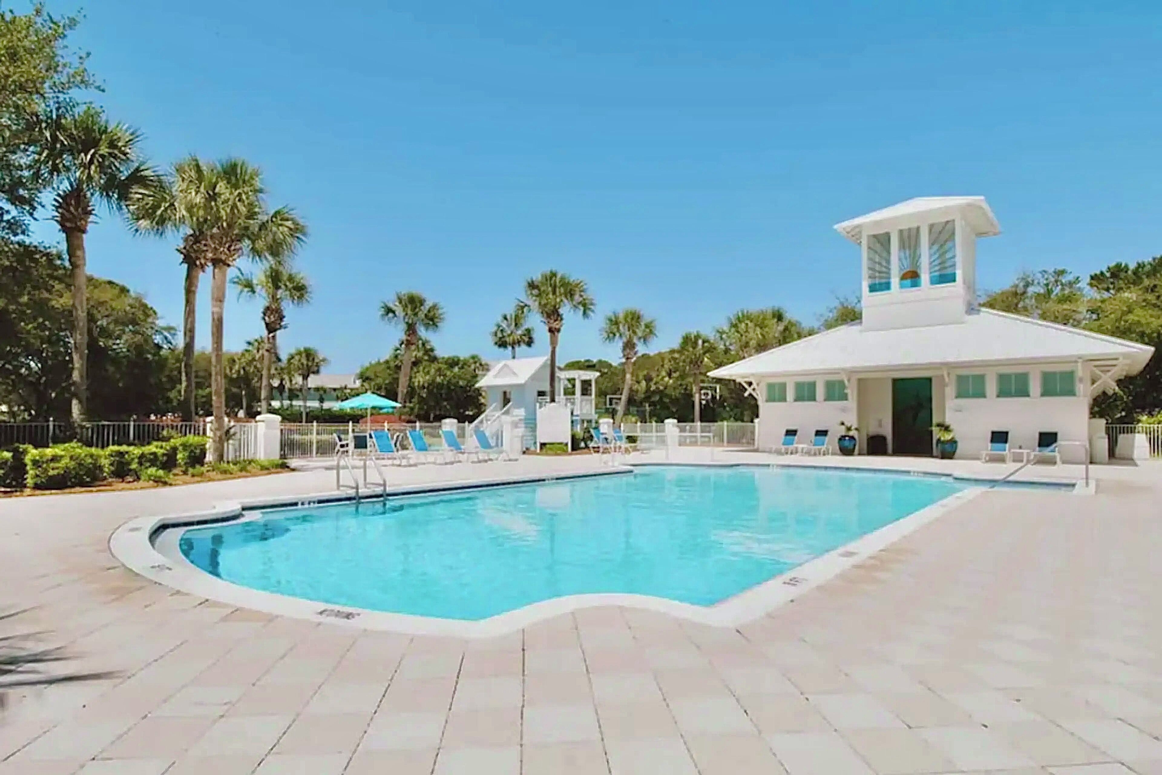 A swimming pool with lounge chairs and a white building with a tower.