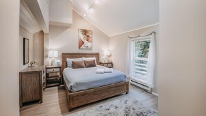 Un dormitorio con una cama grande, mesitas de noche, un velador, un cuadro y una ventana con cortinas.