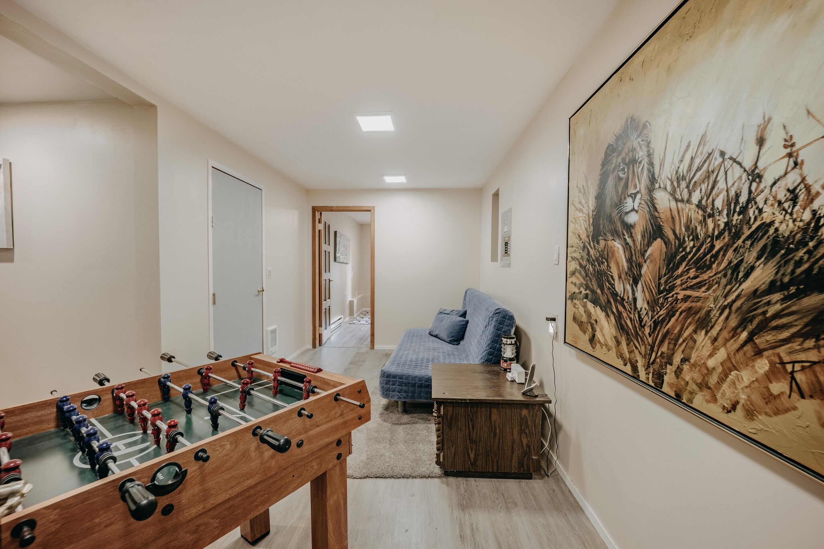 Una habitación con una mesa de fútbol de mesa, un sofá azul y un cuadro grande en la pared.