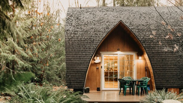 A cozy cabin with a wooden exterior, a porch with green chairs, and a glass door entrance. - 78mbr - Wood Stove - Wifi- Pets Ok - BBQ - Sleeps 6 (Deming)