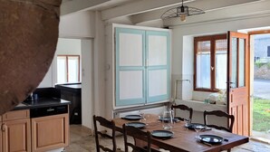 Ein Essbereich mit Holztisch und -stühlen, im Hintergrund eine Küche und ein Fenster mit Blick nach draußen.