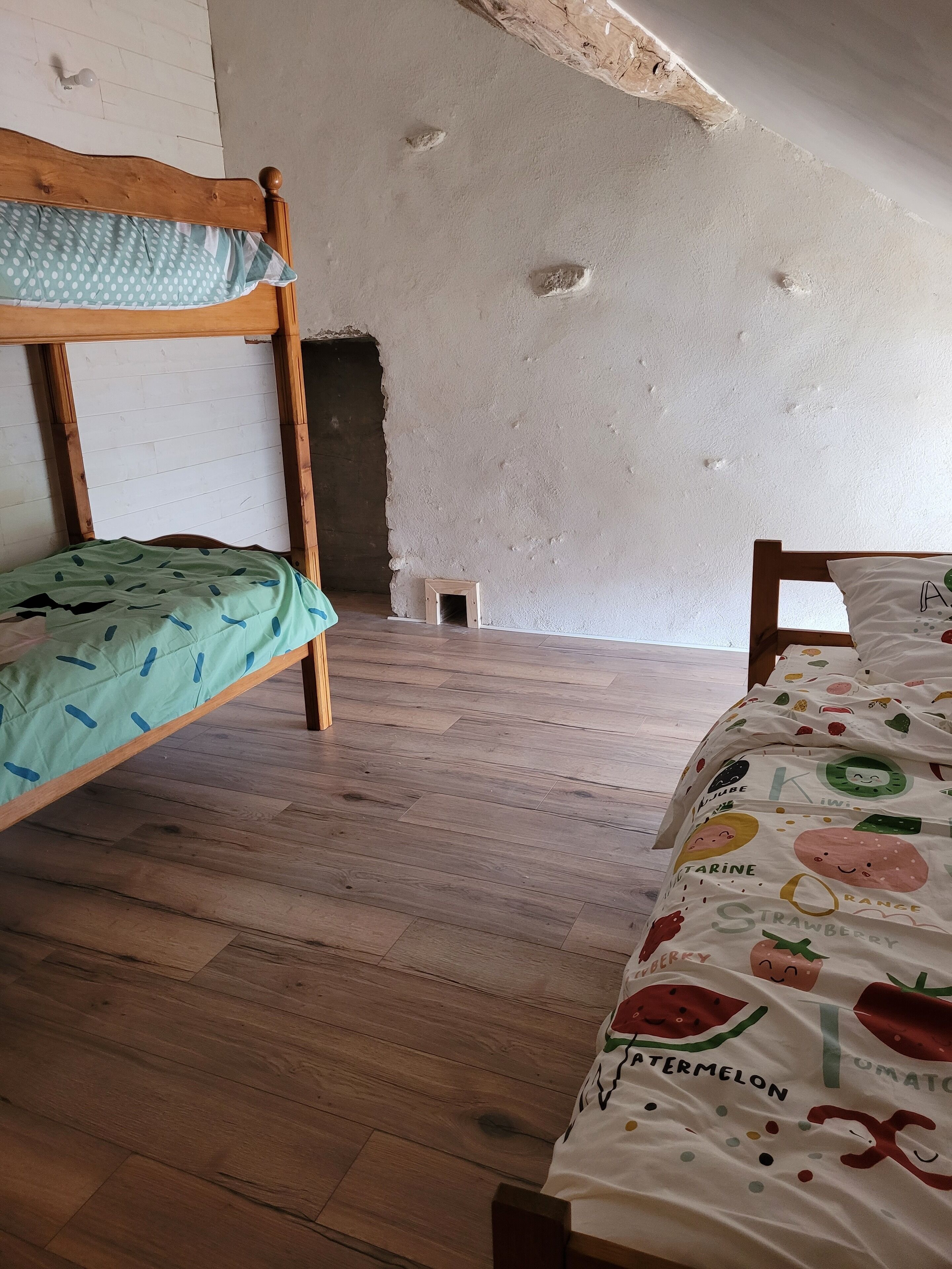 Una stanza con due letti a castello in legno, pavimento in legno e soffitto bianco con segni di usura.