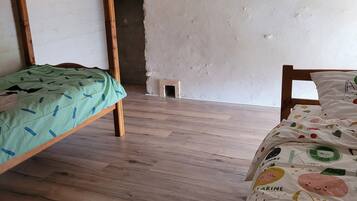 Una stanza con due letti a castello in legno, pavimento in legno e soffitto bianco con segni di usura.