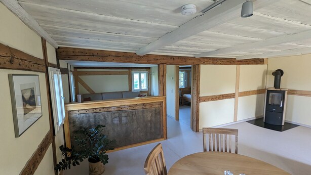A cozy room with a wooden ceiling, a dining table with chairs, a potted plant, and a fireplace.