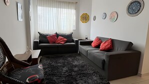 A modern living room with a black sofa, a patterned rug, and decorative plates on the wall. - Cobertura Duplex no Guarujá SP - 4 (Guaruja)