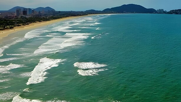 A coastal beach with clear waters and a distant mountain range. - Cobertura Duplex no Guarujá SP - 4 (Guaruja)