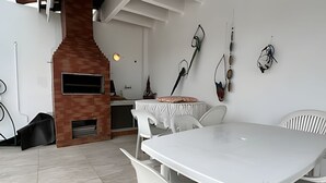 A modern kitchen with a brick oven, white furniture, and decorative wall hangings. - Cobertura Duplex no Guarujá SP - 4 (Guaruja)