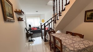 A dining area with a table covered by a patterned tablecloth, wooden chairs, and a staircase leading to another room. - Cobertura Duplex no Guarujá SP - 4 (Guaruja)