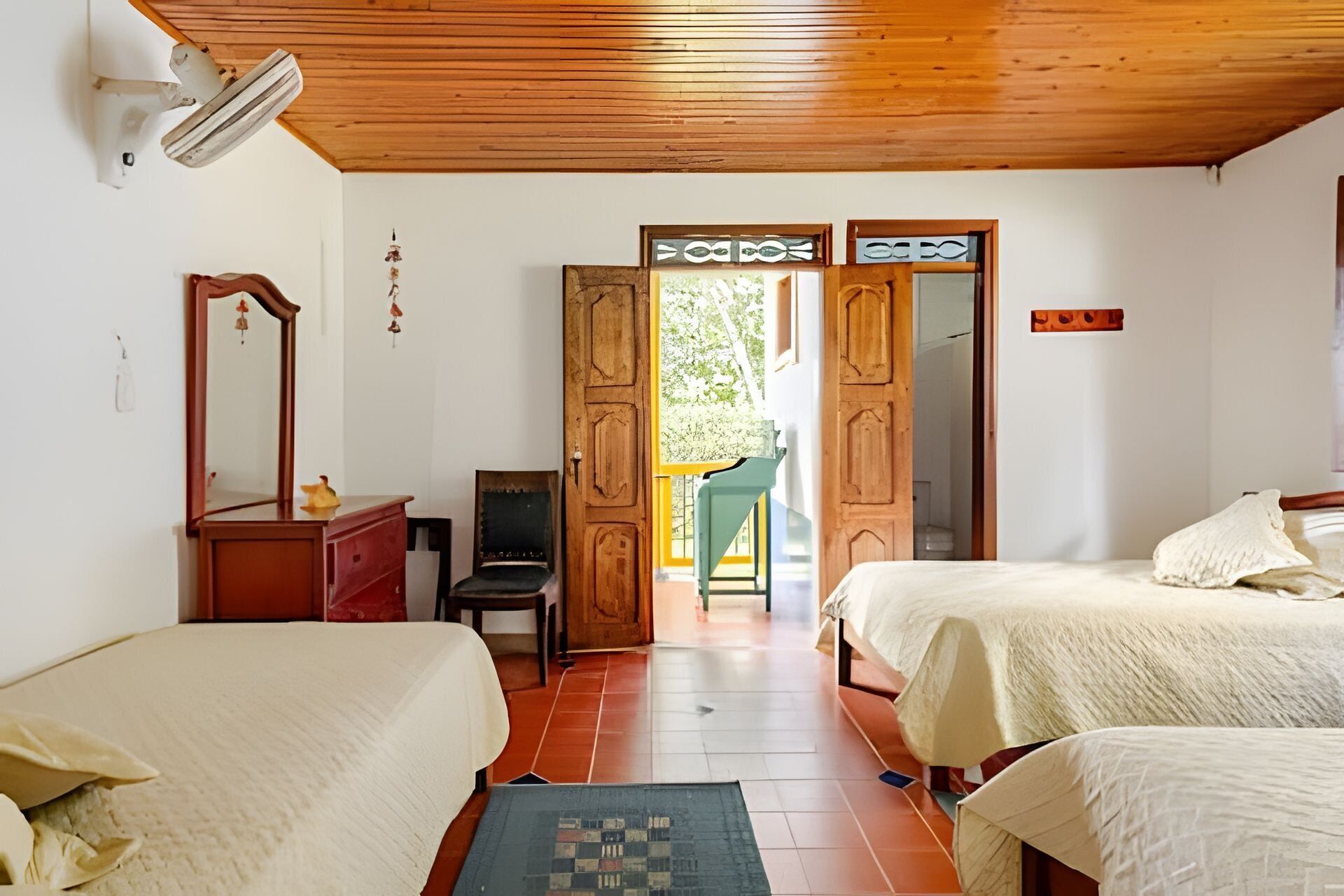 Un dormitorio con dos camas, techo de madera, un espejo y una puerta que da al exterior.